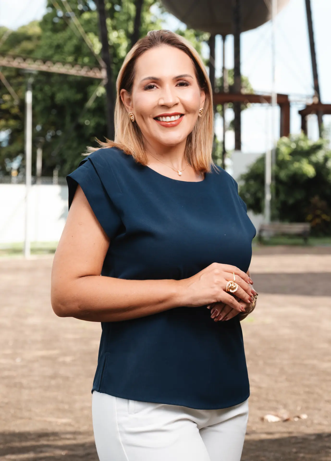 Dra. Tânia Sena sorrindo com blusa azul e calça branca em ambiente externo